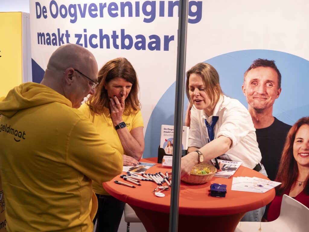 een medewewrker van de Oogvereniging geeft uitleg aan een statafel