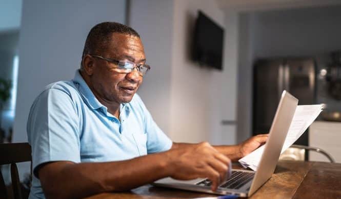 een man met bril op doet zijn digitale zaken op een laptop aan de eetkamertafel