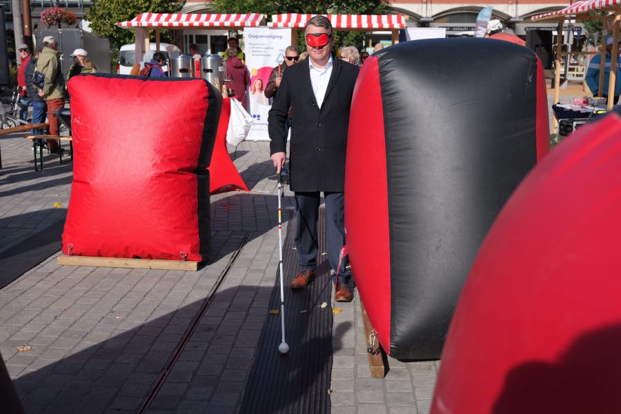 Wethouder Jan Broekema loopt geblinddoekt met een witte stok door een obstakelparcours