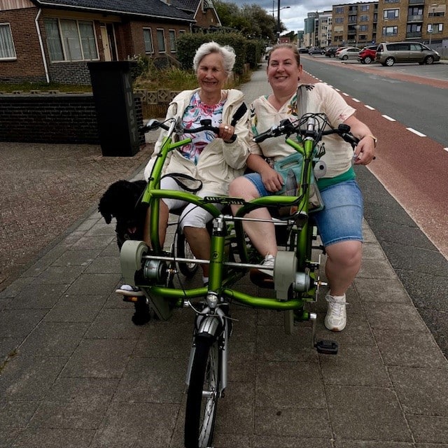 twee vrouwen op een duofiets, ze pauzeren op een stoepje en lachen